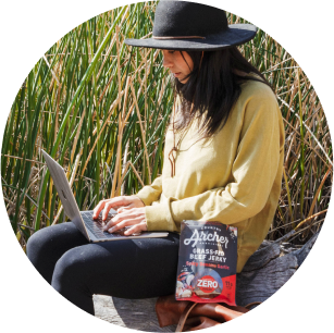 girl on laptop in a field with package of Country Archer Beef Jerky